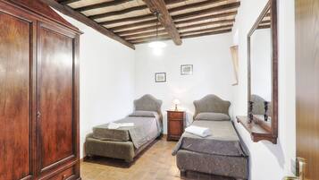 Un dormitorio con dos camas individuales, un armario de madera, una mesita de noche con una lámpara y un espejo en la pared.