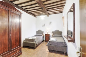 A bedroom with two single beds, a wooden wardrobe, a nightstand with a lamp, and a mirror on the wall.
