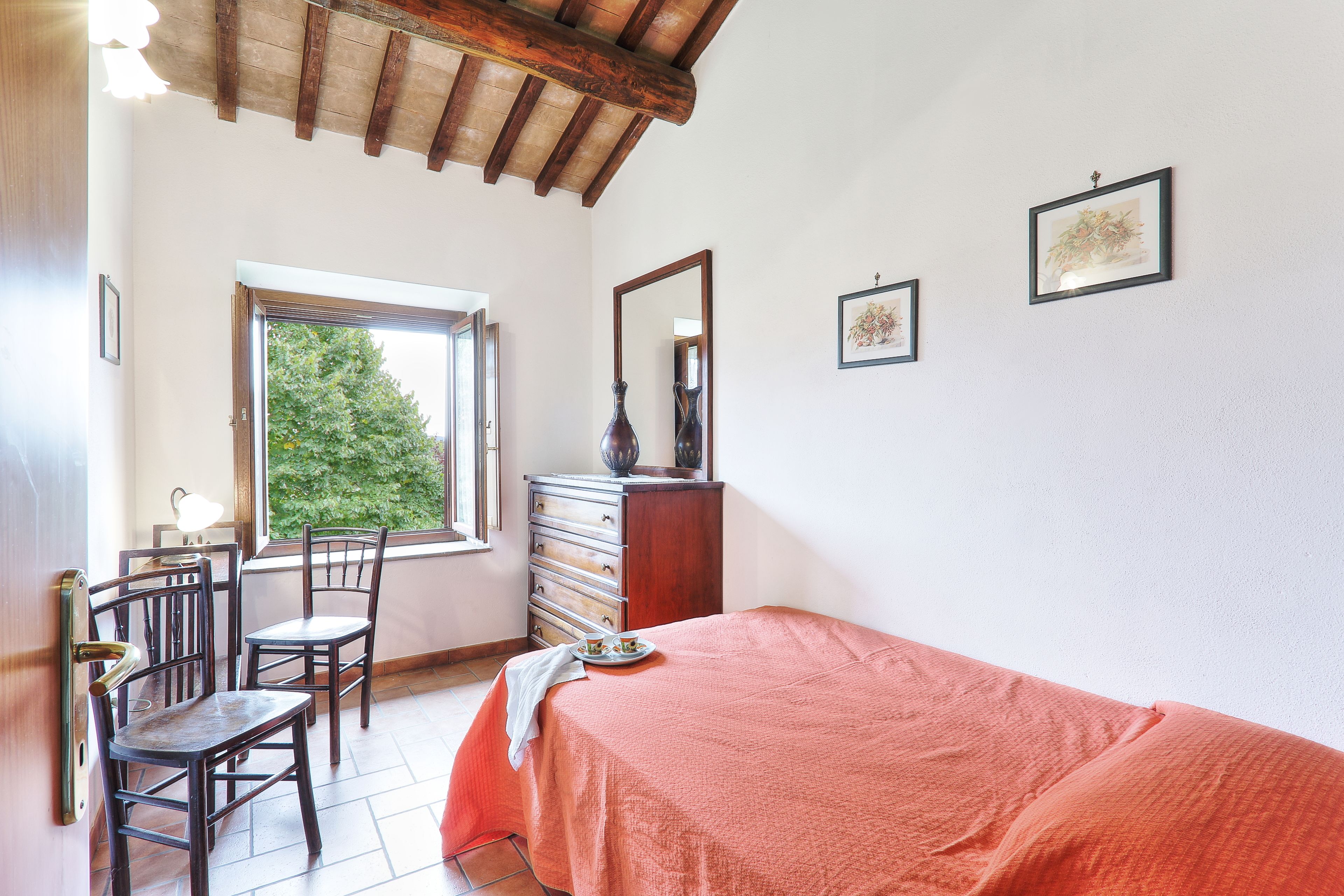 A bedroom with a bed, two chairs, a dresser, and a window.