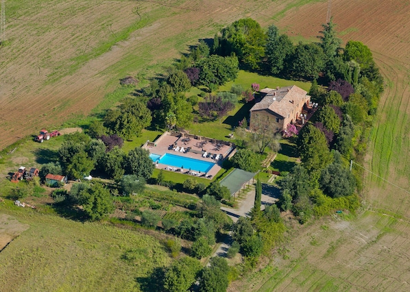 An aerial view of a property with a swimming pool, a stone building, and surrounding fields.