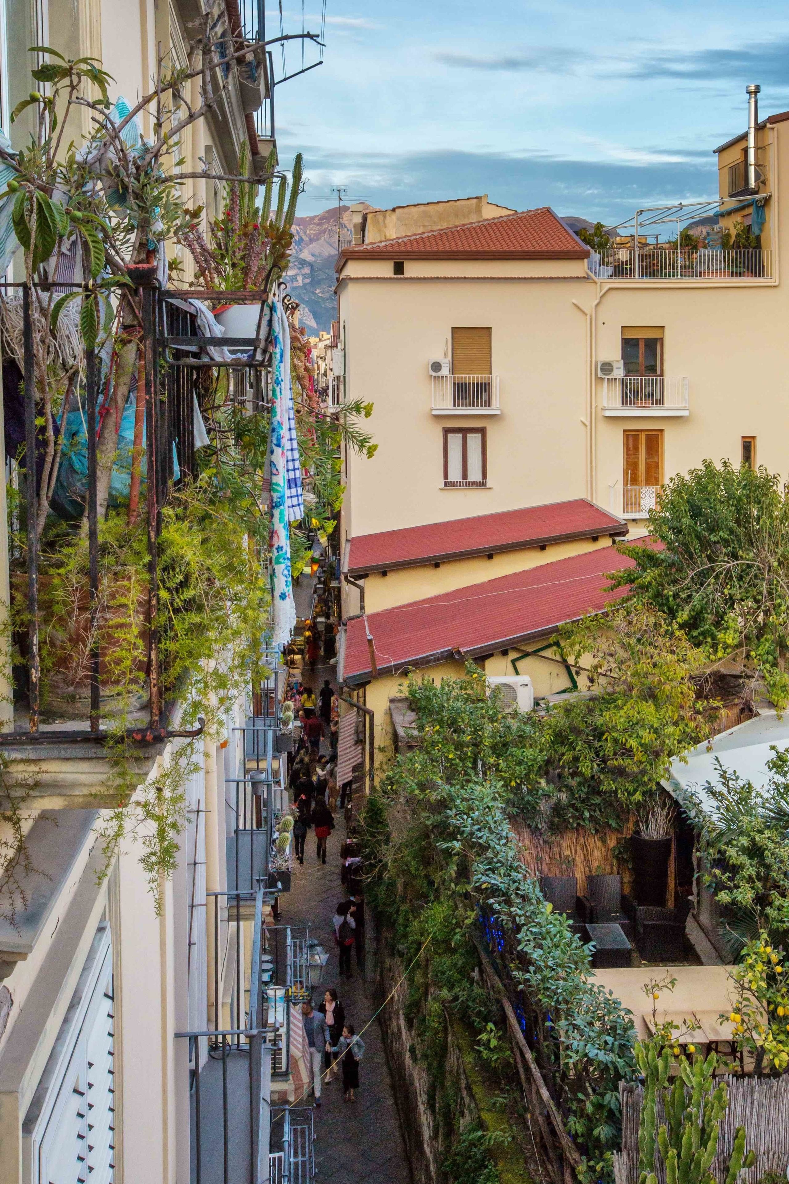 A narrow alleyway between buildings with balconies, some with plants and decorations.