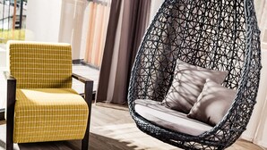 Een kamer met een geel geruit fauteuil en een zwarte hangstoel van geweven materiaal, voorzien van kussens.