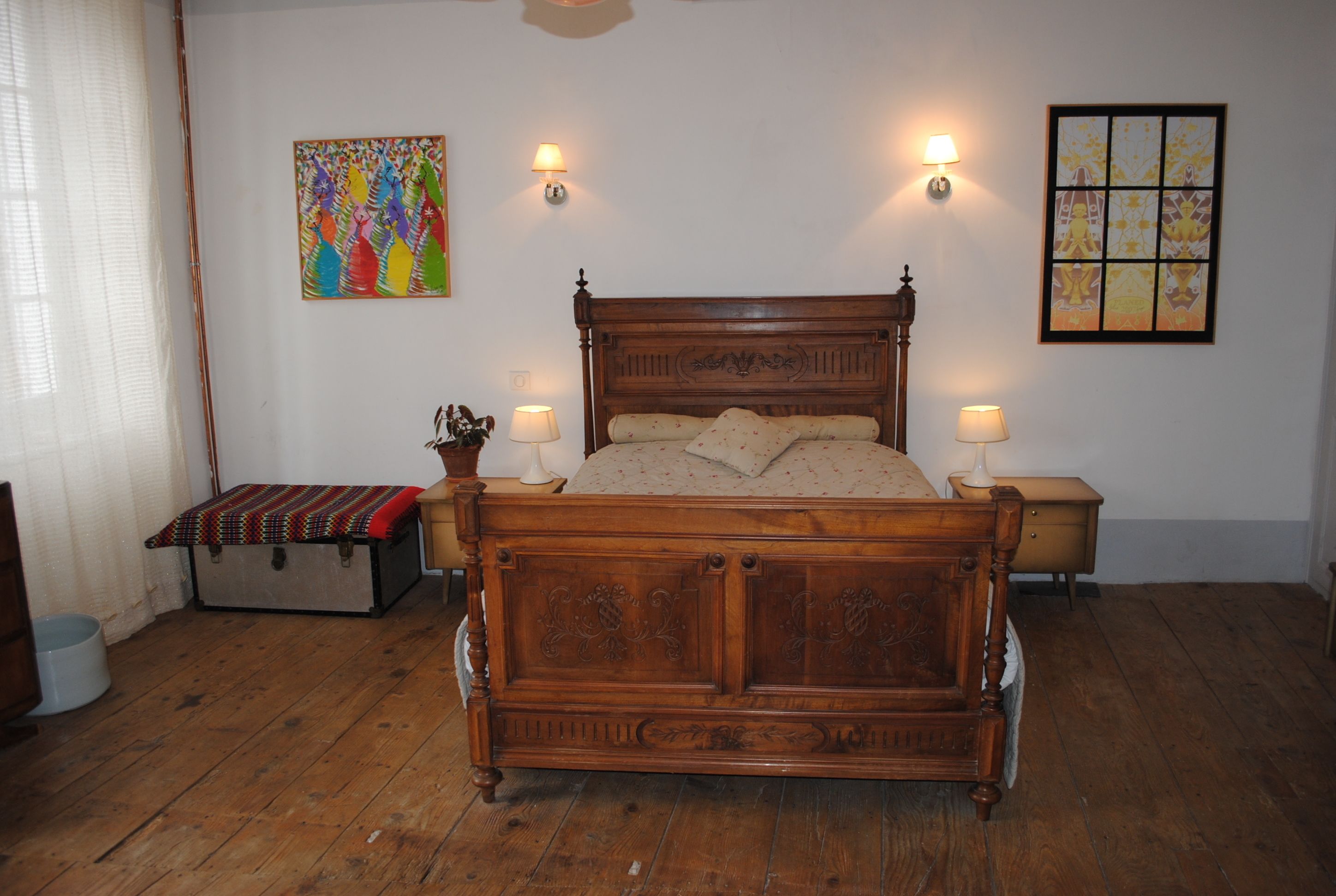 A wooden bed with a headboard, two bedside lamps, and a colorful painting on the wall.