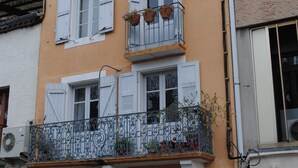 Un edificio de dos pisos con un balcón, una puerta y una ventana con contraventanas.