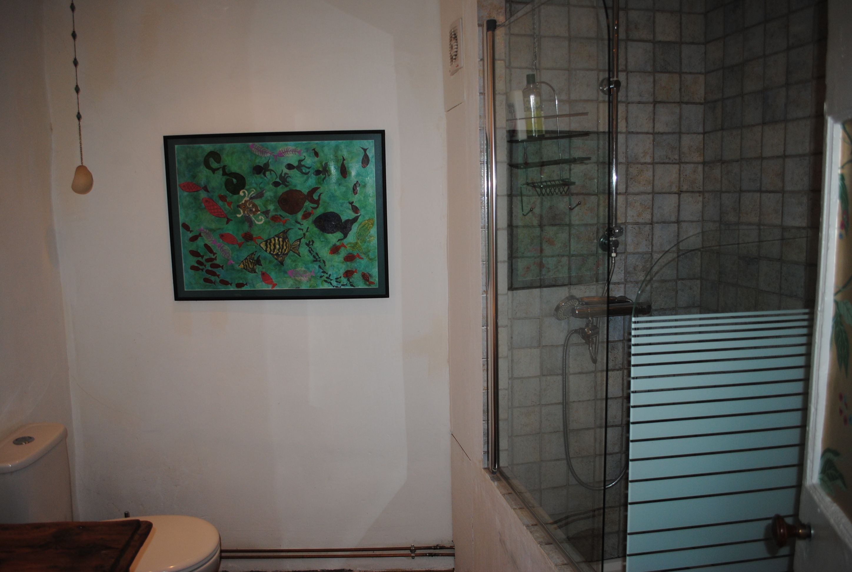Un baño con cabina de ducha de vidrio, una obra de arte enmarcada en la pared y un asiento de váter de madera.