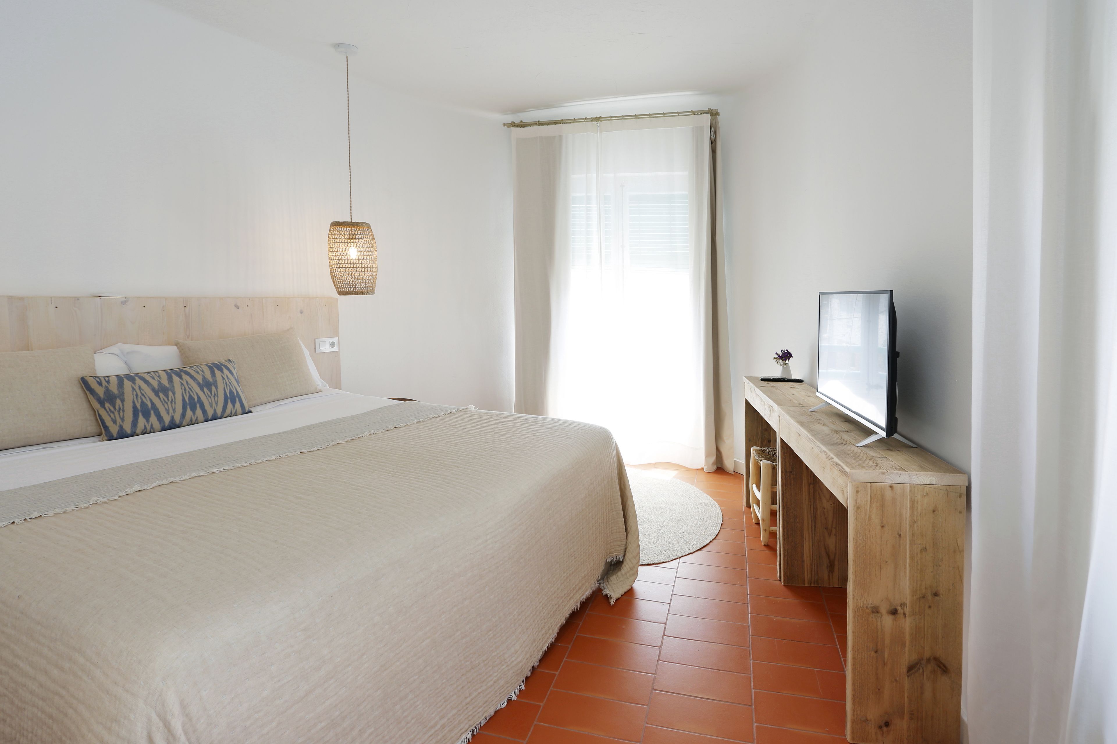 Een slaapkamer met een bed, een televisie op een houten standaard en een raam met gordijnen.