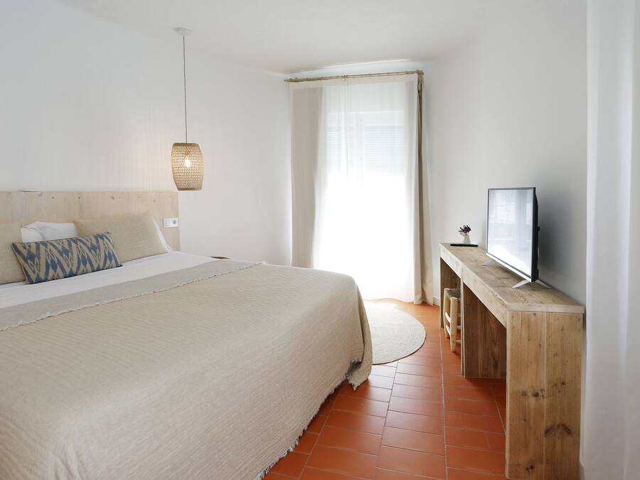 A bedroom with a bed, a television on a wooden stand, and a window with curtains.