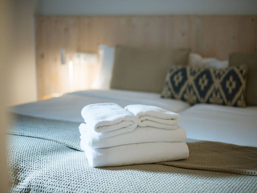 A neatly made bed with a folded white towel on a textured bedspread, a wooden headboard, and patterned pillows.