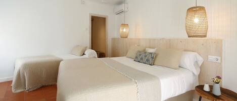 A bedroom with two beds, a wooden headboard, a small table with a vase, and hanging lights.