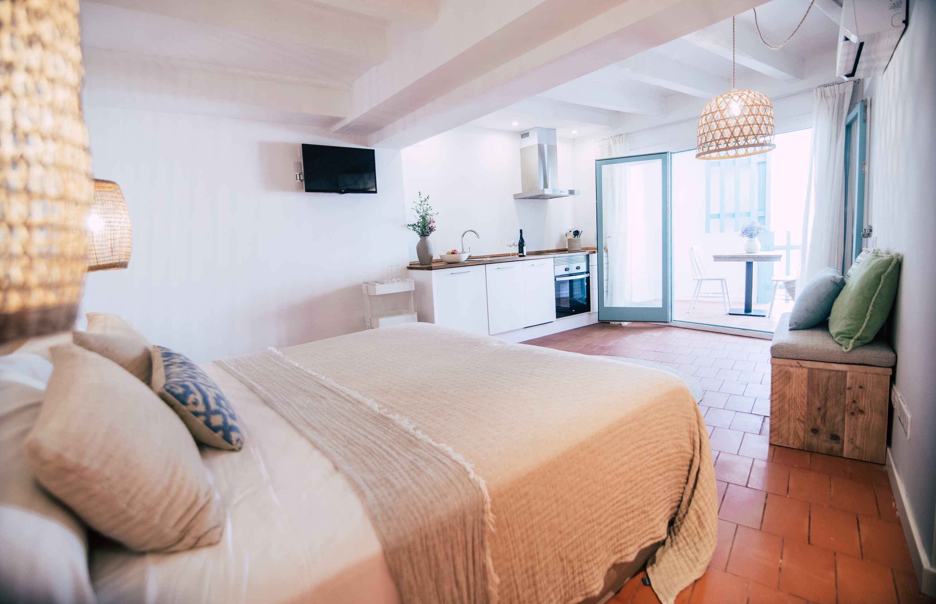 Un dormitorio con una cama grande, un banco de madera con cojines y vistas a la cocina y al balcón.