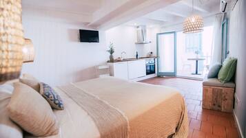 Un dormitorio con una cama grande, un banco de madera con cojines y vistas a la cocina y al balcón.