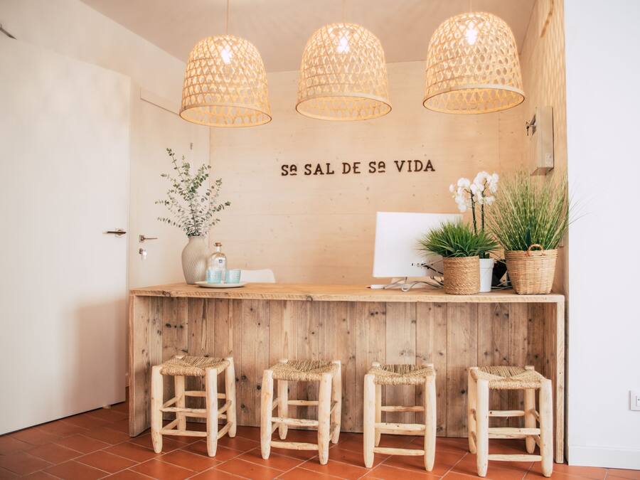 A wooden reception desk with three wicker chairs, a potted plant, and a wall-mounted sign reading "SAL DE SAL VIDA".