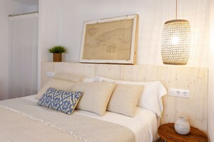 A bedroom with a bed, a map on the wall, a hanging light, a small plant, and a vase on a nightstand.