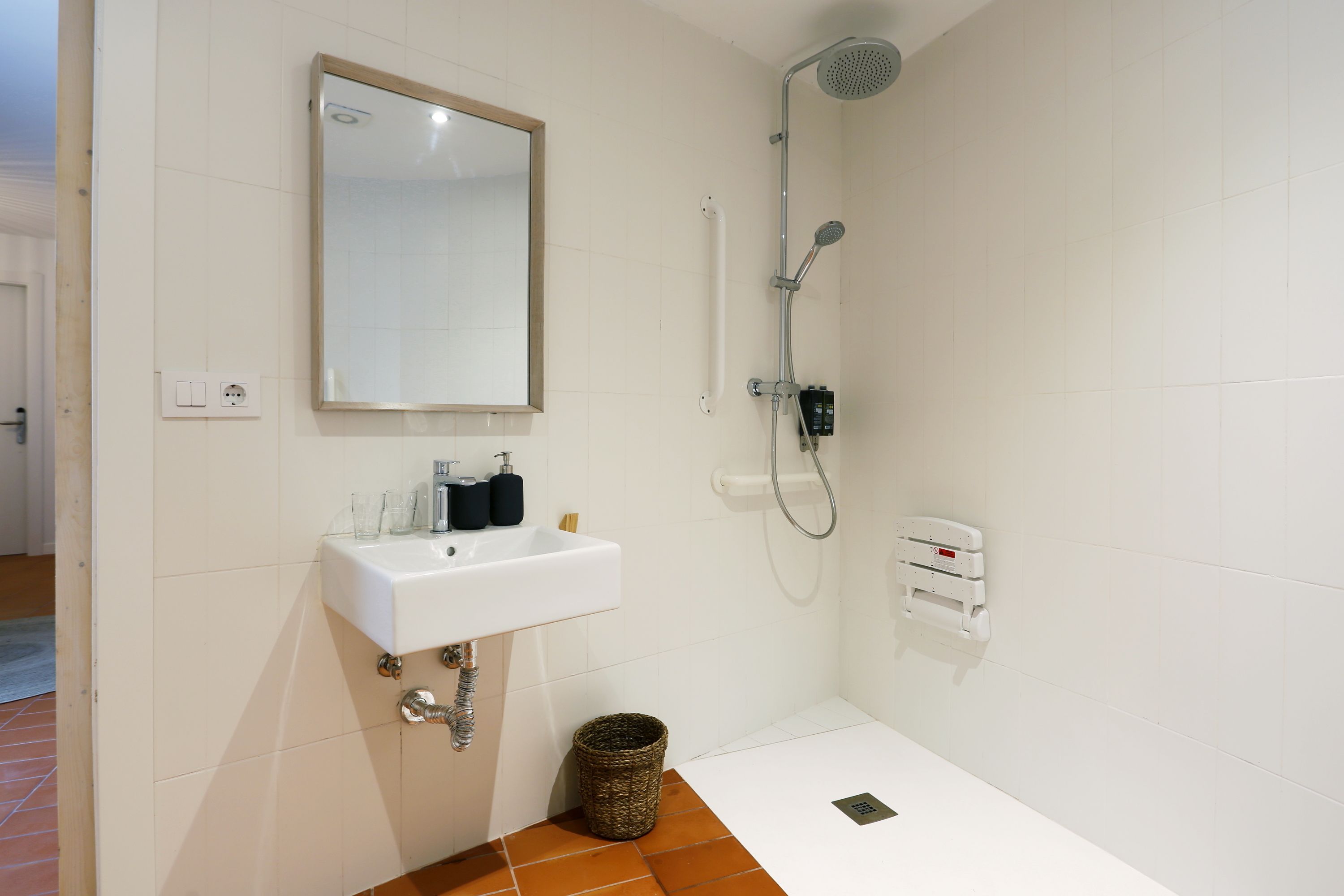 Un baño con lavamanos blanco, espejo, ducha y un pequeño cubo de basura.