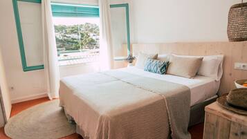 A bedroom with a large bed, a window with curtains, a wooden headboard, and a wicker lamp.