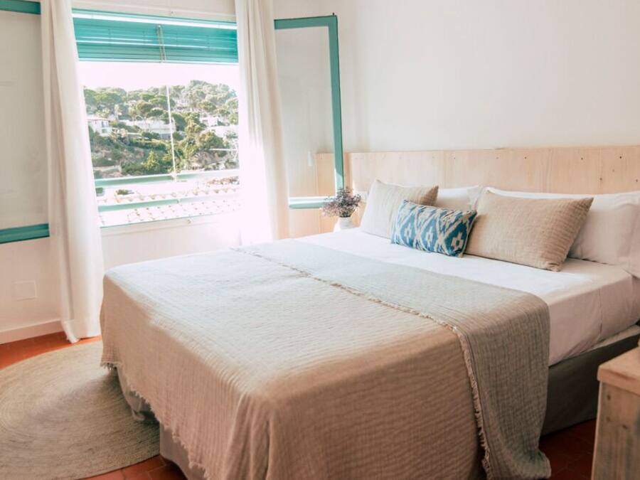 A bedroom with a large bed, a window with curtains, a wooden headboard, and a wicker lamp.