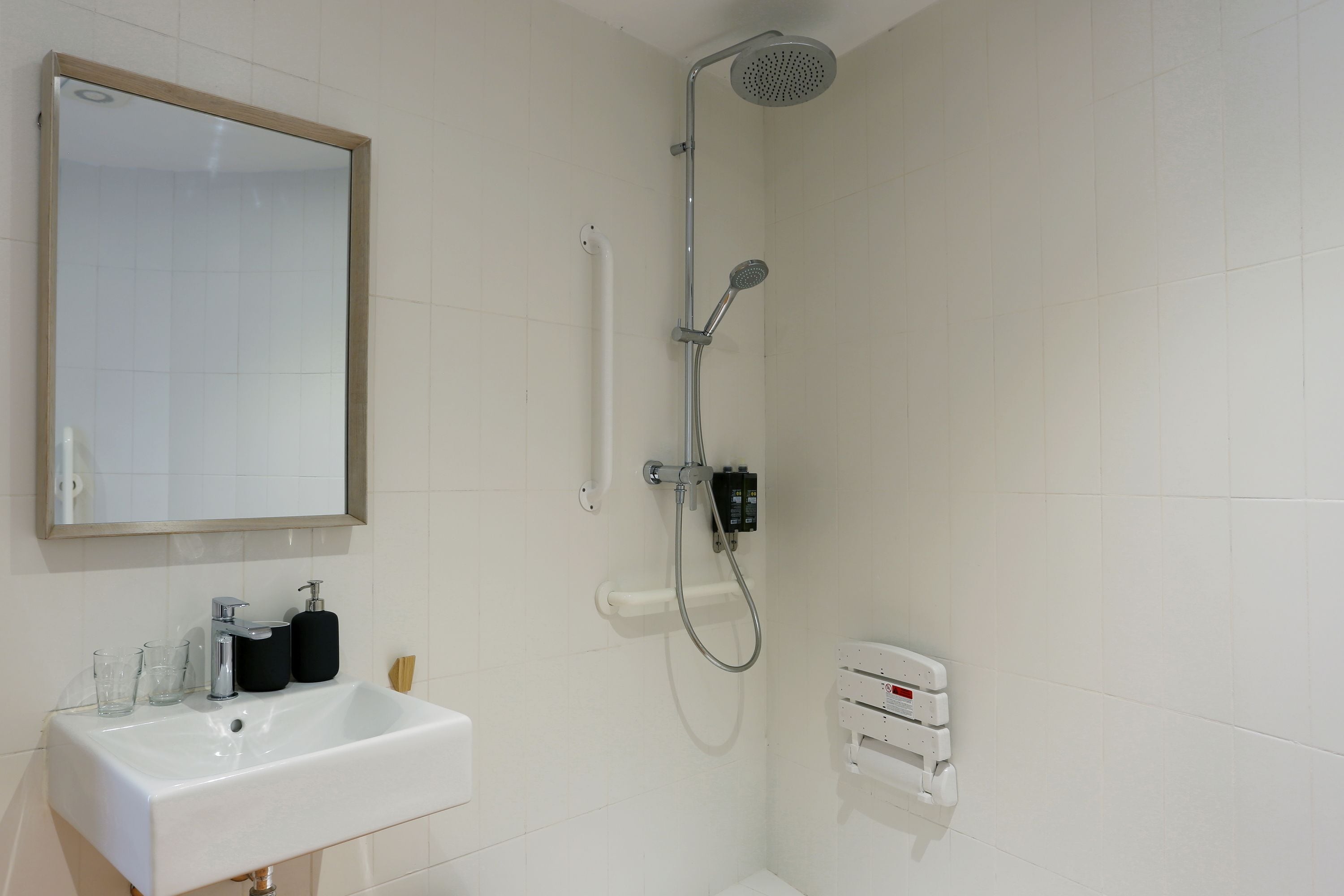 Un baño con lavamanos blanco, espejo, ducha y toallero.