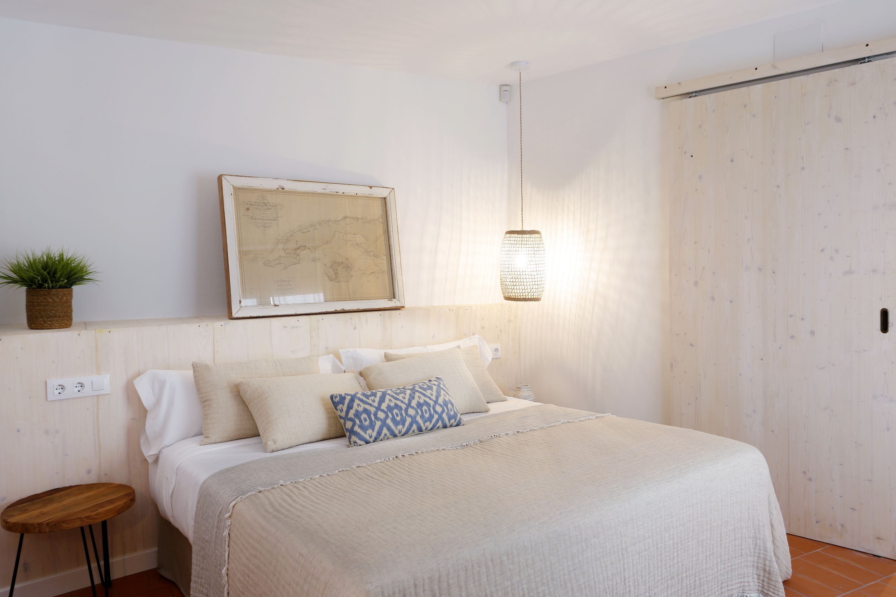A bedroom with a bed, a hanging light, a map on the wall, and a small stool.