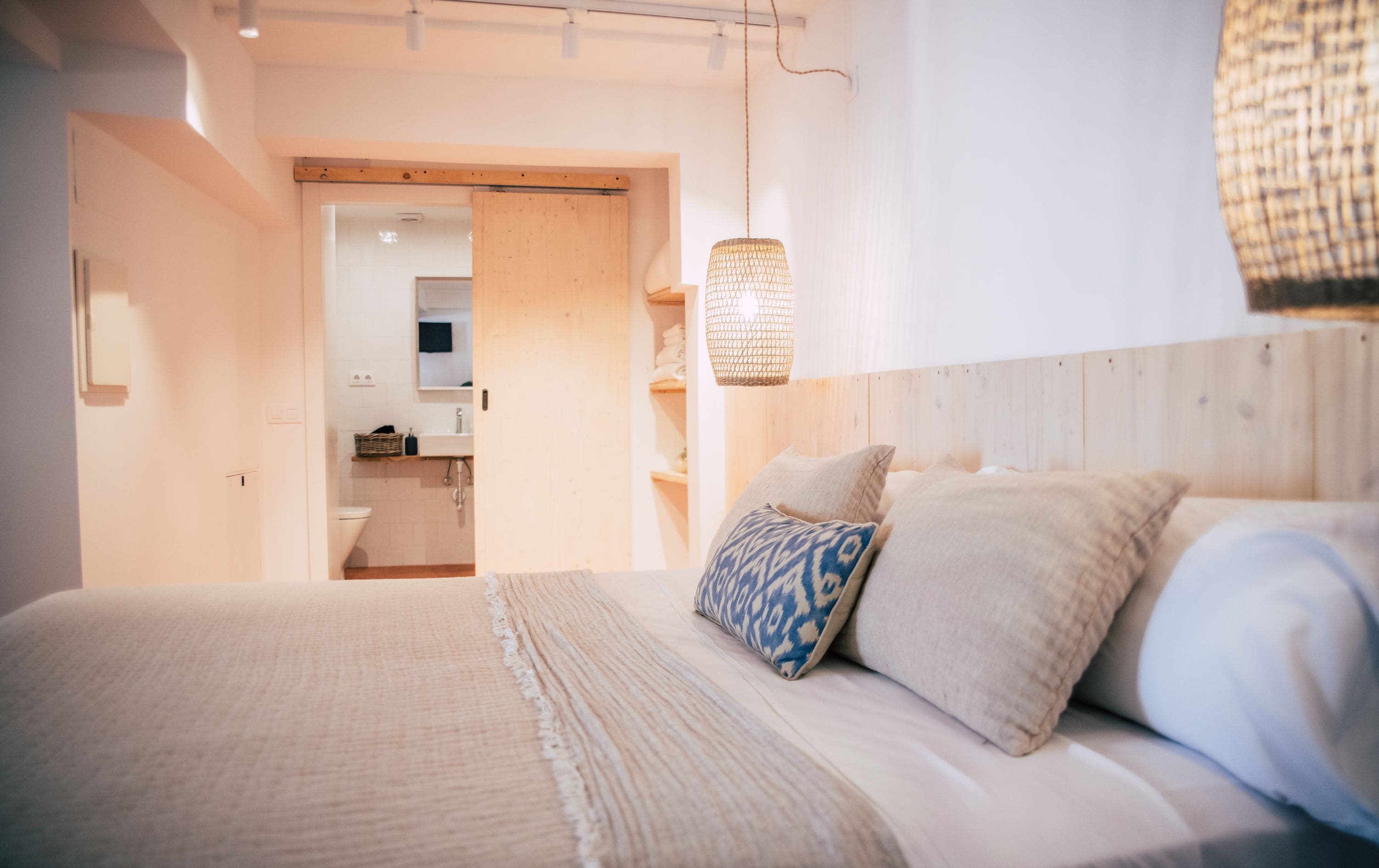 Un dormitorio con cama, almohadas, una lámpara colgante y vistas al baño.