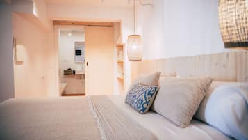 A bedroom with a bed, pillows, a hanging light fixture, and a view into the bathroom.