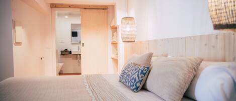 Un dormitorio con cama, almohadas, una lámpara colgante y vistas al baño.