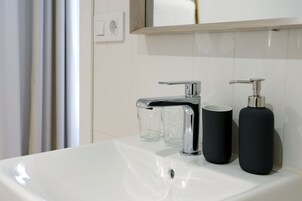 Un baño con un lavamanos blanco, dos vasos de vidrio y dos botellas negras.