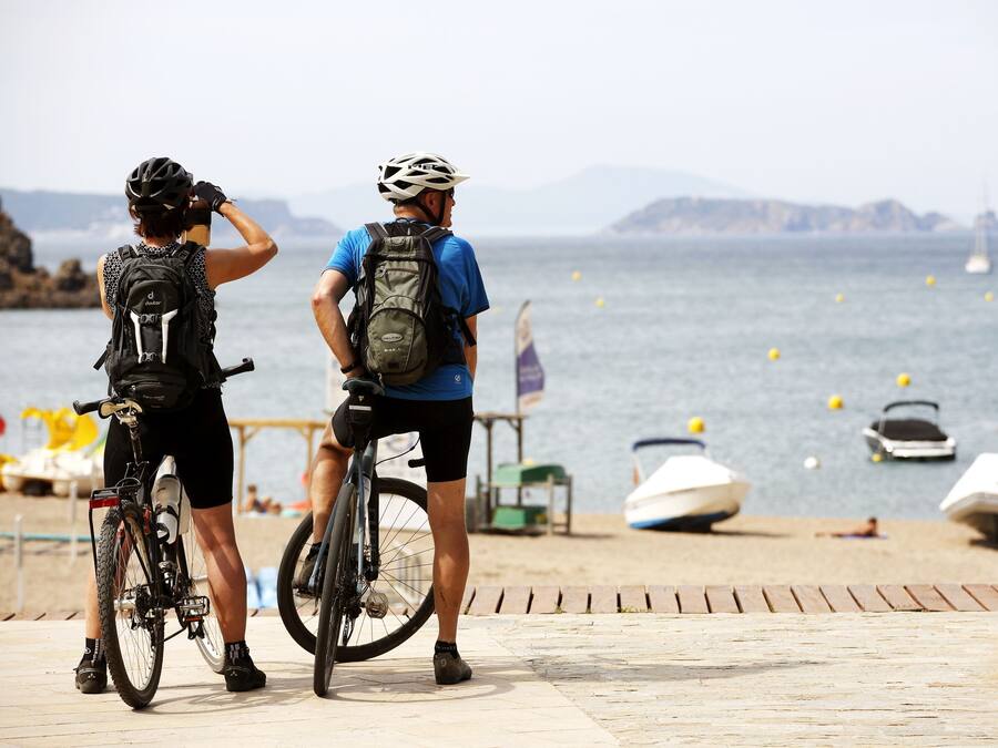 Twee fietsers op een houten looppad aan de zee, met boten op de achtergrond.