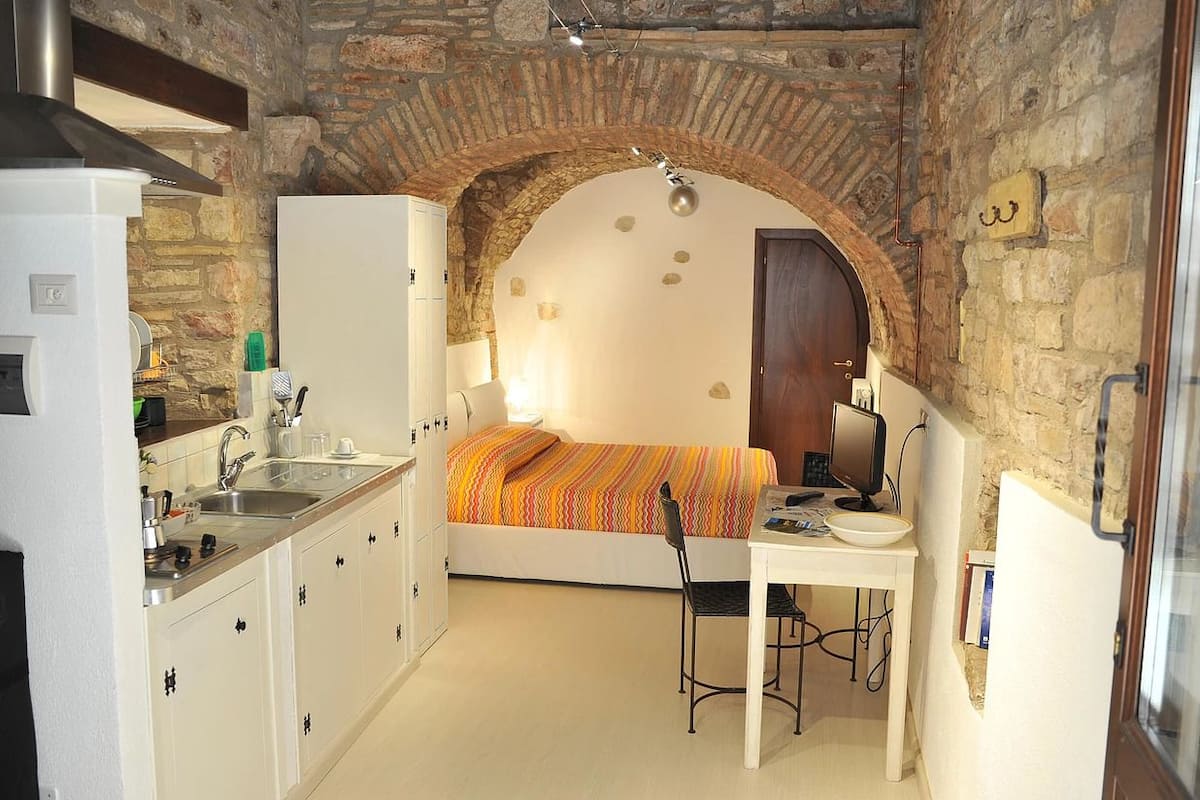 A compact room with a bed, a desk, and a kitchenette.