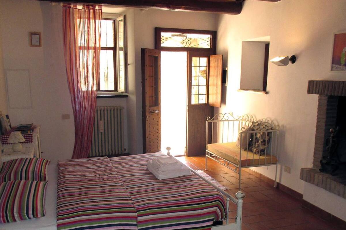 A bedroom with a bed, a radiator, a window with curtains, a mirror, and a fireplace.