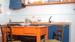 A kitchen with a dining table and chairs, a gas stove, a sink, and various kitchen items on the countertop. - Vico Del Poeta (Assisi)