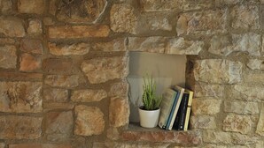 A stone wall with a small shelf holding a potted plant and books. - Vico Del Poeta (Assisi)