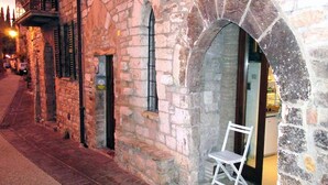 A stone building with arched doorways and a white chair outside. - Vico Del Poeta (Assisi)