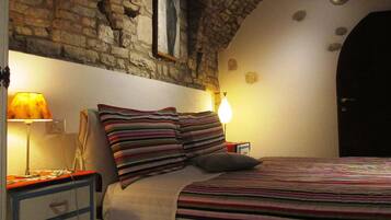 Una camera da letto con parete in pietra, un letto con lenzuola a righe, due lampade ai piedi del letto e un comodino con una lampada.