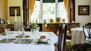 A dining room with a table set for a meal, a window with curtains, and framed pictures on the walls. - Kiltariff Hall Country House (Newry)