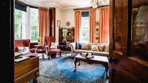 A traditional room with a large window, a sofa, a chair, a table, and a wooden cabinet. - Kiltariff Hall Country House (Newry)
