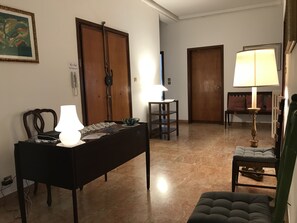 Una sala de estar con un sofá, una mesa con lámpara, una silla y una puerta de madera.