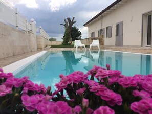 Una piscina con dos sillas blancas y flores rosadas al frente.