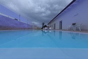 A swimming pool with a clear blue water surface, surrounded by a high fence and a building with a sloped roof. - Ofra Matera (Matera)