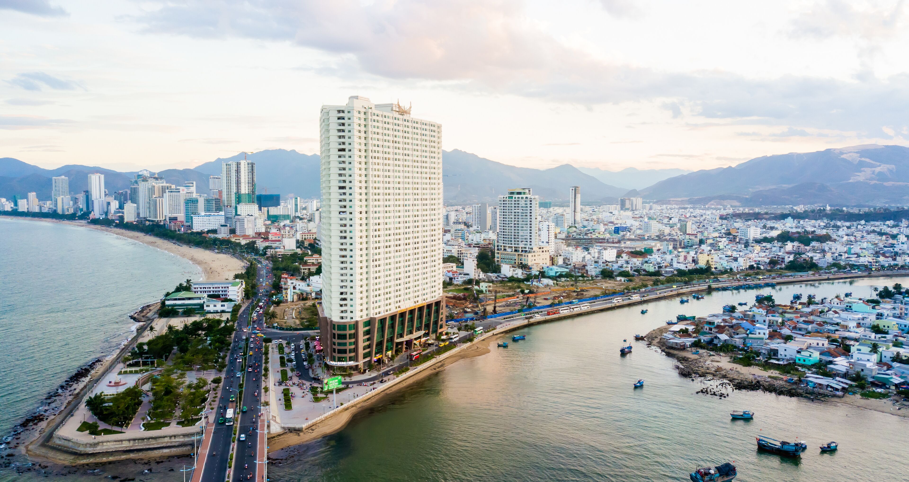 A coastal cityscape with a prominent high-rise hotel, a marina, and a beach.