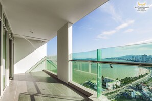 A balcony with a glass railing overlooking a beach and cityscape. - Muong Thanh Luxury Khanh Hoa Hotel (Nha Trang)