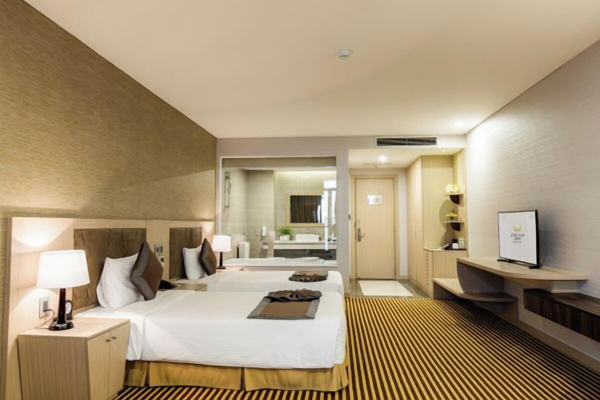 Une chambre d’hôtel avec deux lits, un grand miroir, une télévision et un petit bureau avec une lampe.