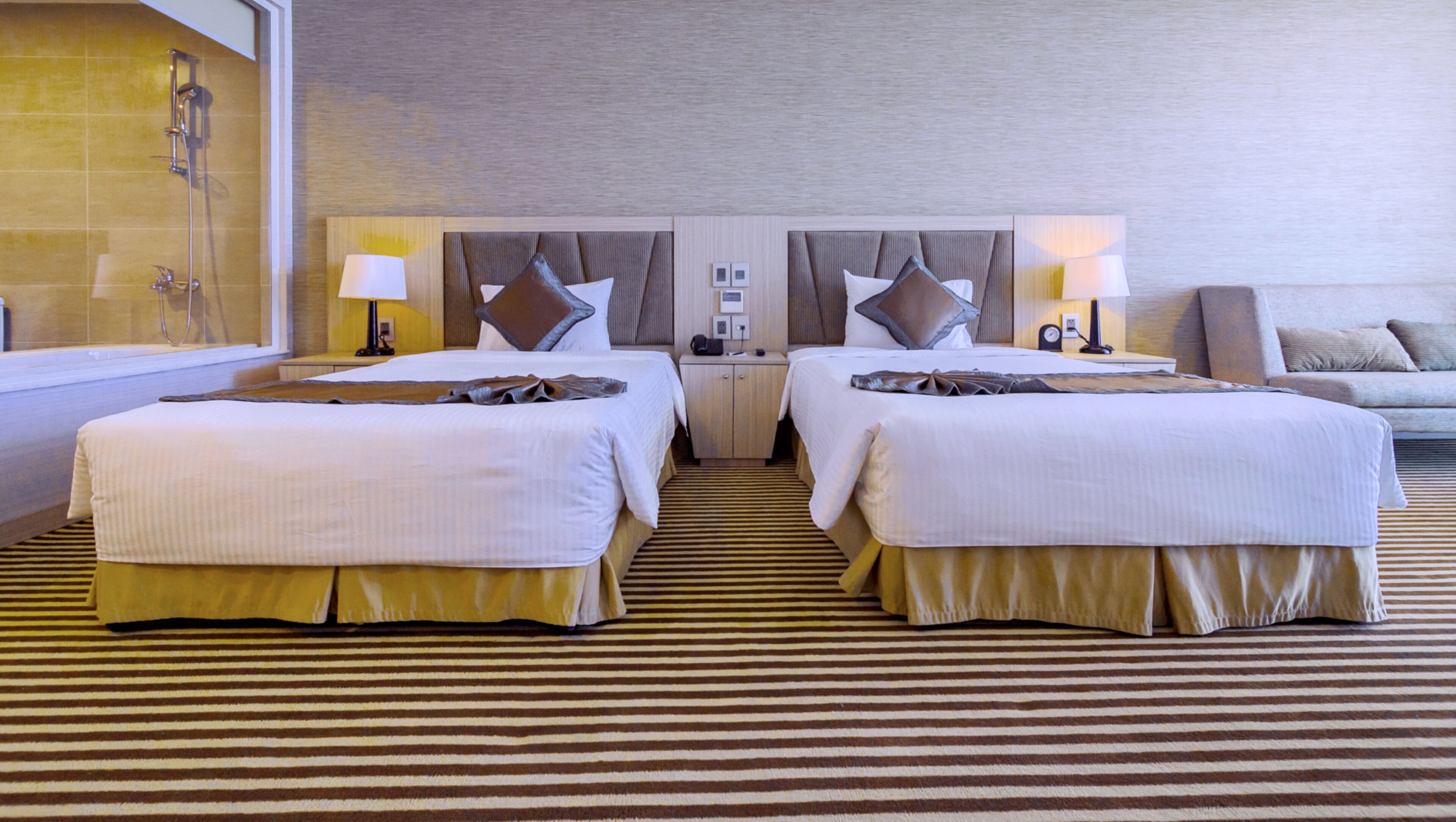 Ein Hotelzimmer mit zwei Betten, einem Schlafsofa, einem kleinen Tisch und einem Badezimmer mit Dusche.