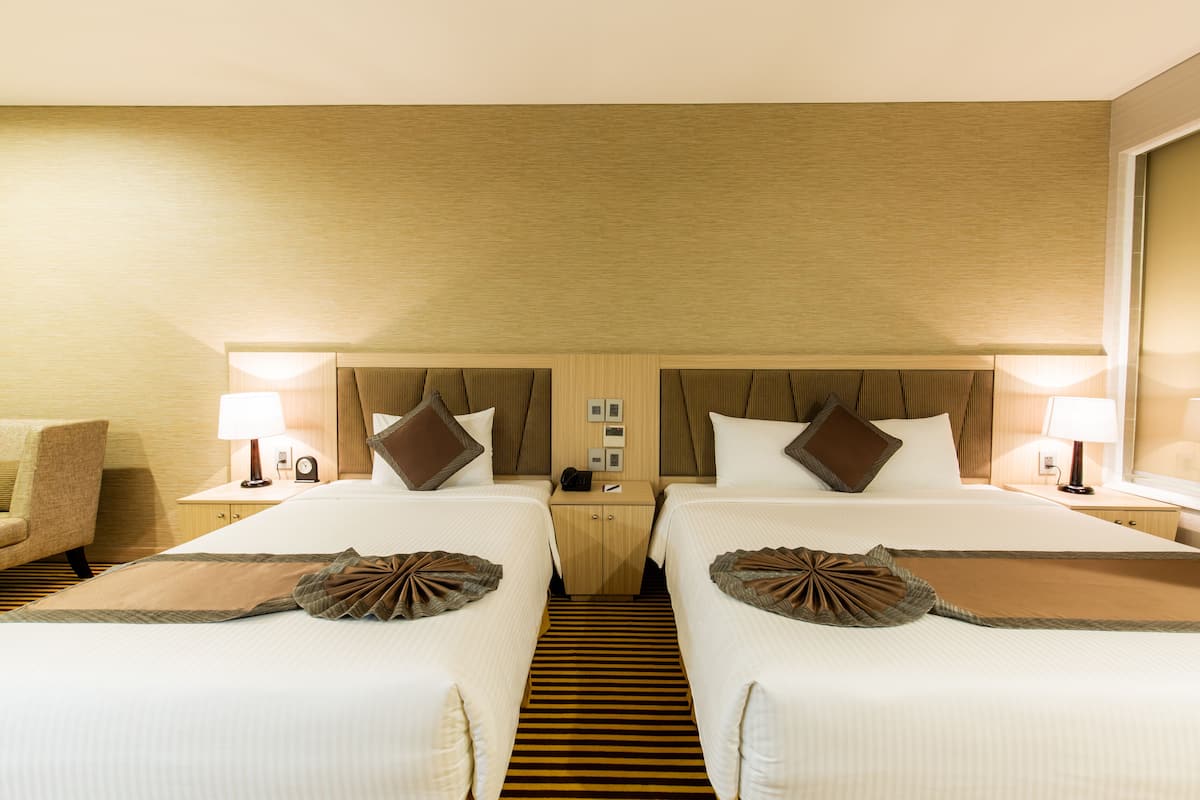 A hotel room with two beds, a nightstand, a lamp, a chair, and a striped carpet.