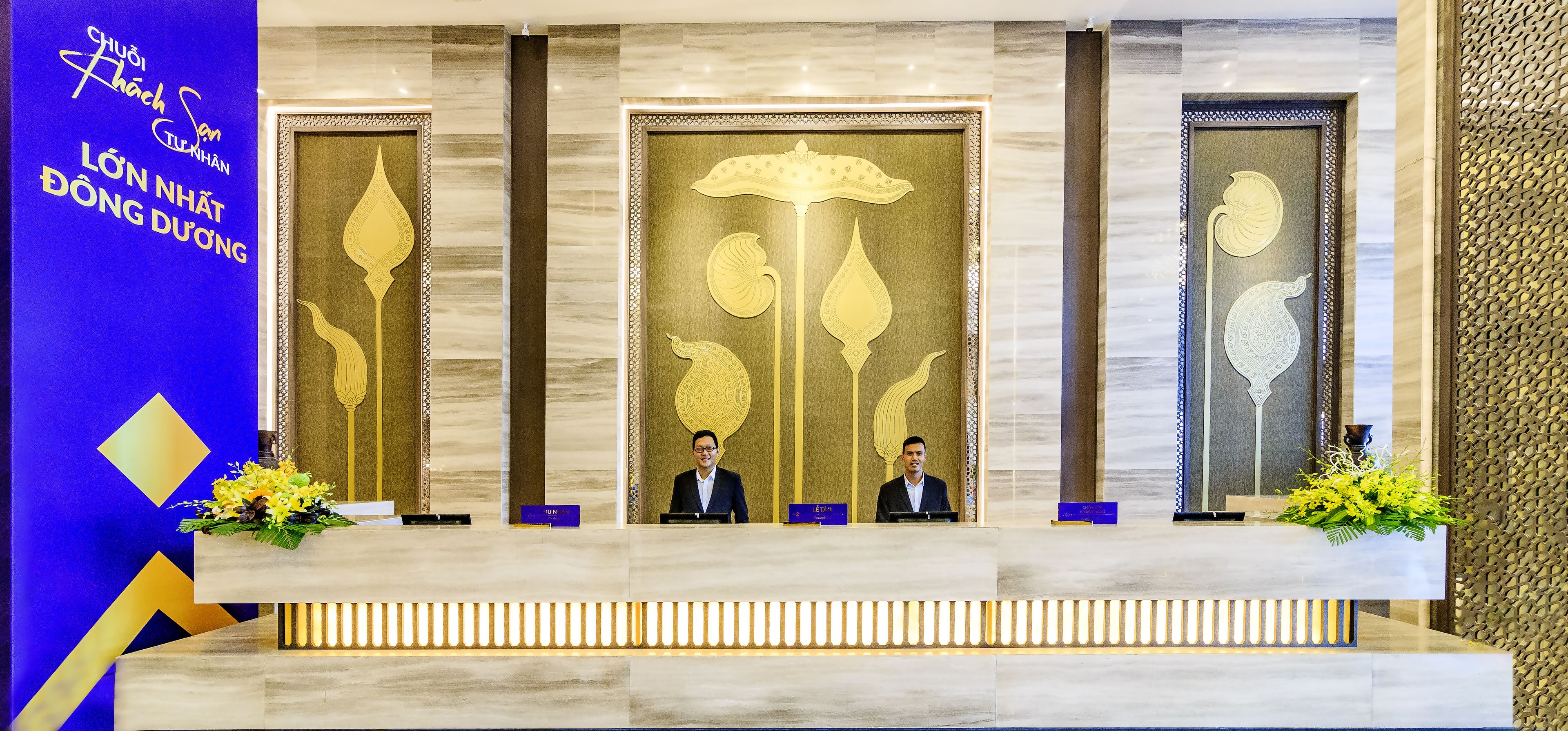 A reception desk with three receptionists, a blue pillar with text, and decorative panels with golden designs.