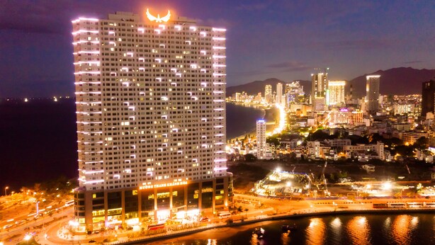 A high-rise hotel with a distinctive rooftop design, surrounded by a cityscape with a river and other buildings. - Muong Thanh Luxury Khanh Hoa Hotel (Nha Trang)