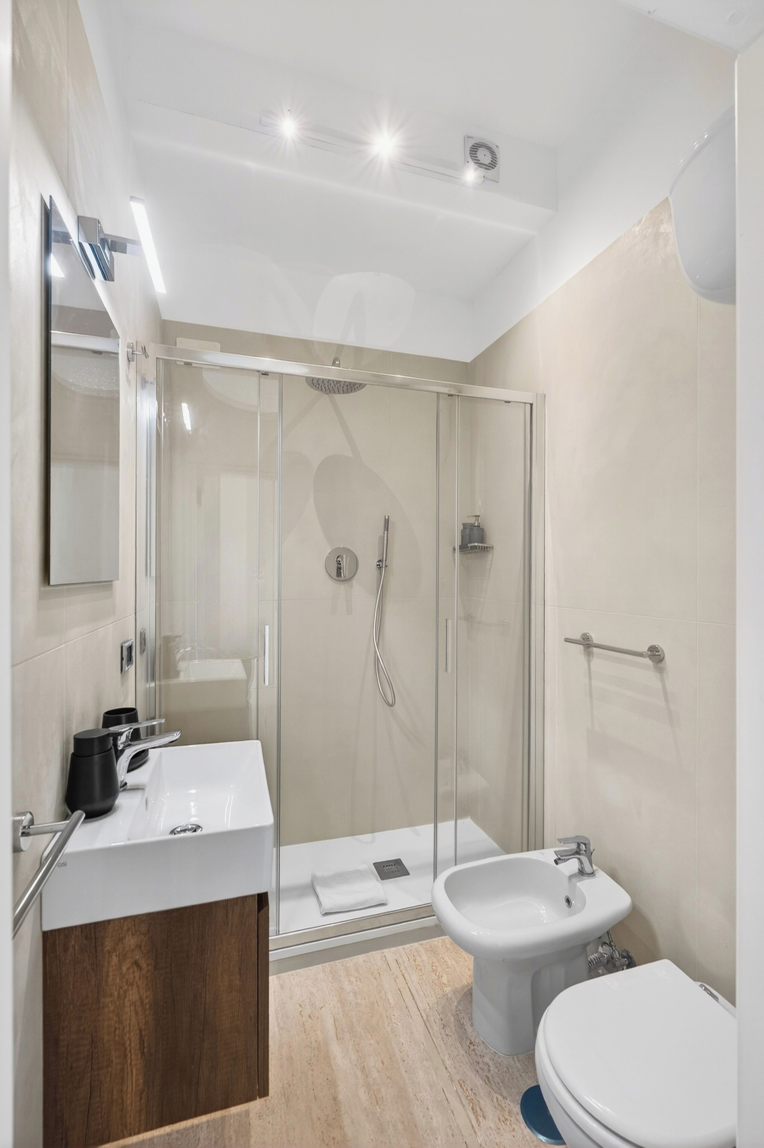 A modern bathroom with a glass-enclosed shower, a white sink, and a bidet.