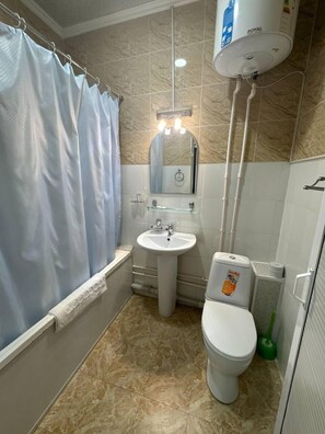 A bathroom with a shower curtain, sink, mirror, toilet, and a water heater.
