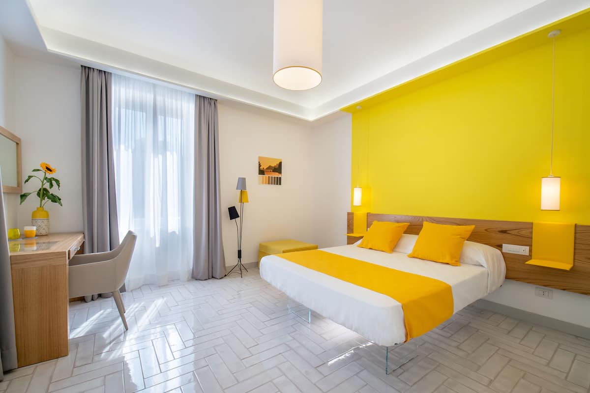 A hotel room with a bed, a desk, a chair, a lamp, and a window with curtains.