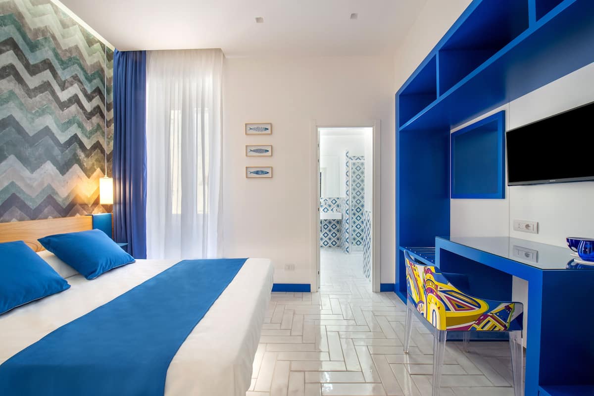 A hotel room with a bed, a desk, a TV, and a bathroom visible through an open door.