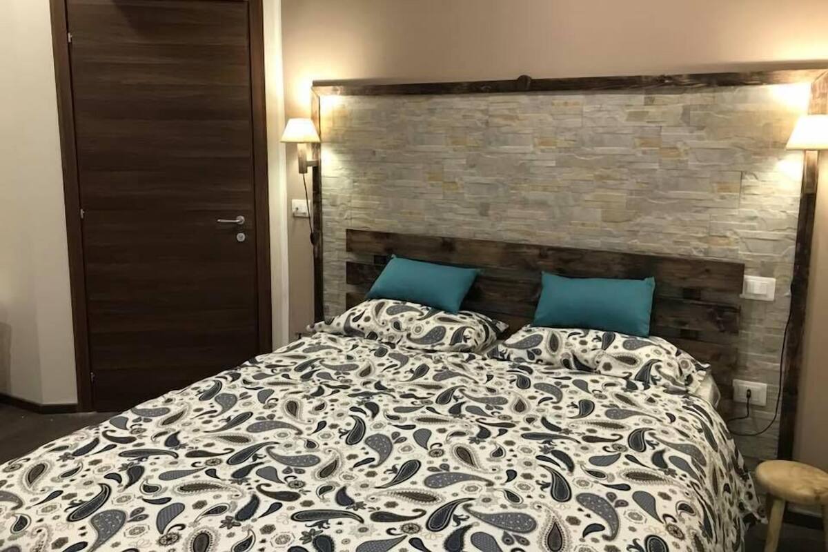 Quarto com cama, porta de madeira e parede de pedra.